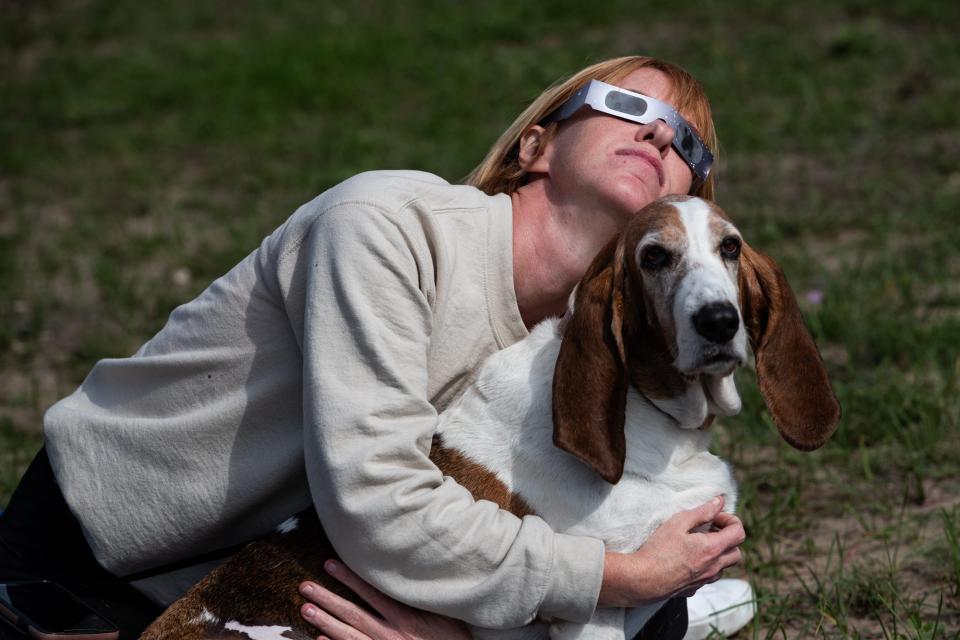 A Houston woman holds her basset hound and watches the annular solar eclipse at Lake Corpus Christi State Park on Saturday, Oct. 14, 2023, in Mathis, Texas.