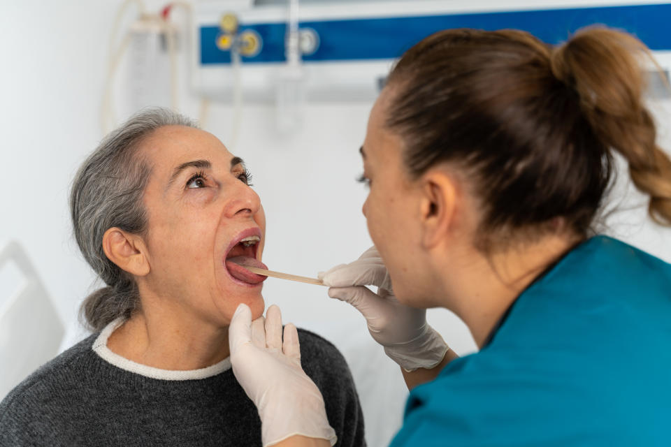 A patient has her throat examined by a healthcare professional using a tongue depressor