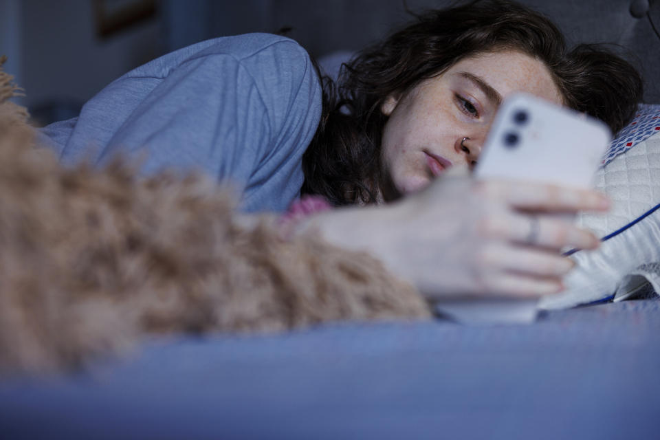 Woman lying in bed, looking at her smartphone closely