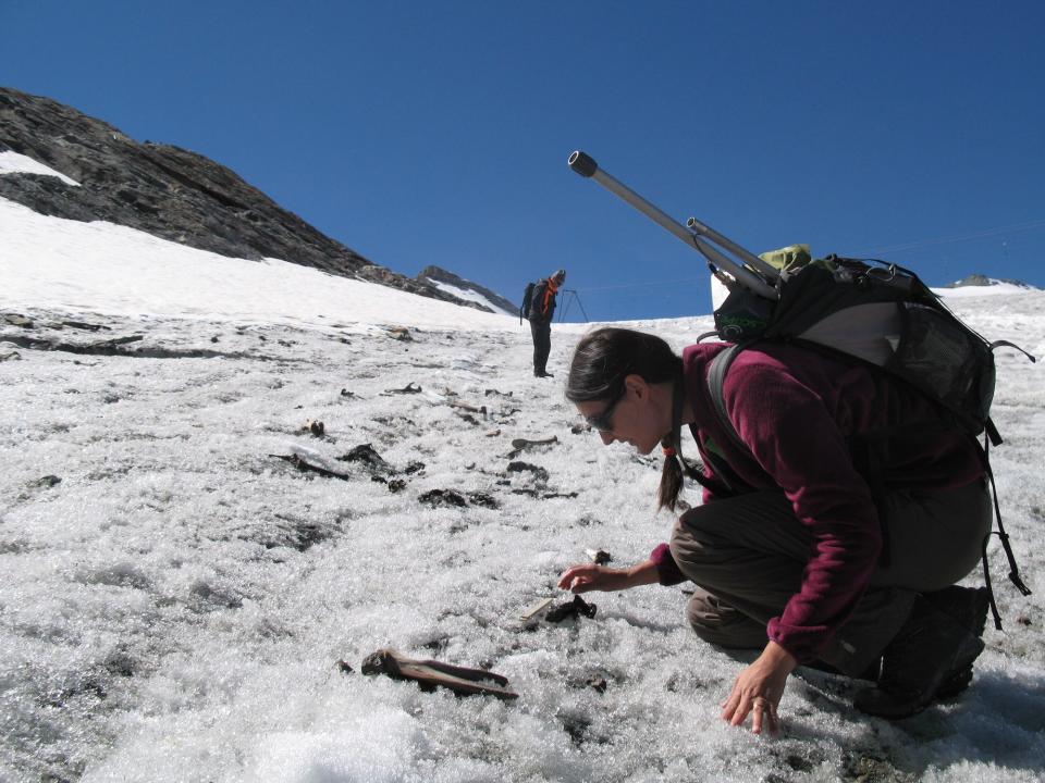 A woman wearing a large backpack crouching on icy ground and looking at a bone.