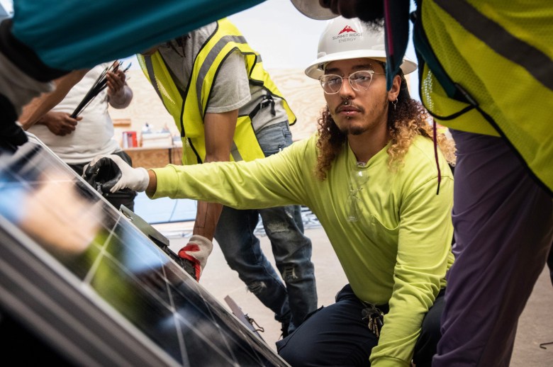 Moises Vega III, leveling solar panel for placement onto a pitched, shingled, mocked-up roof.