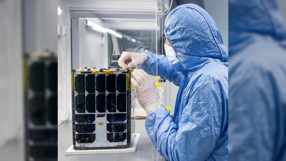 A researcher in a protective suit stood next to the ACS3 CubeSat