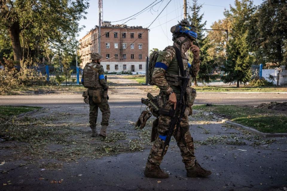 A pair of Ukrainian soldiers walking with a brick building behind them.