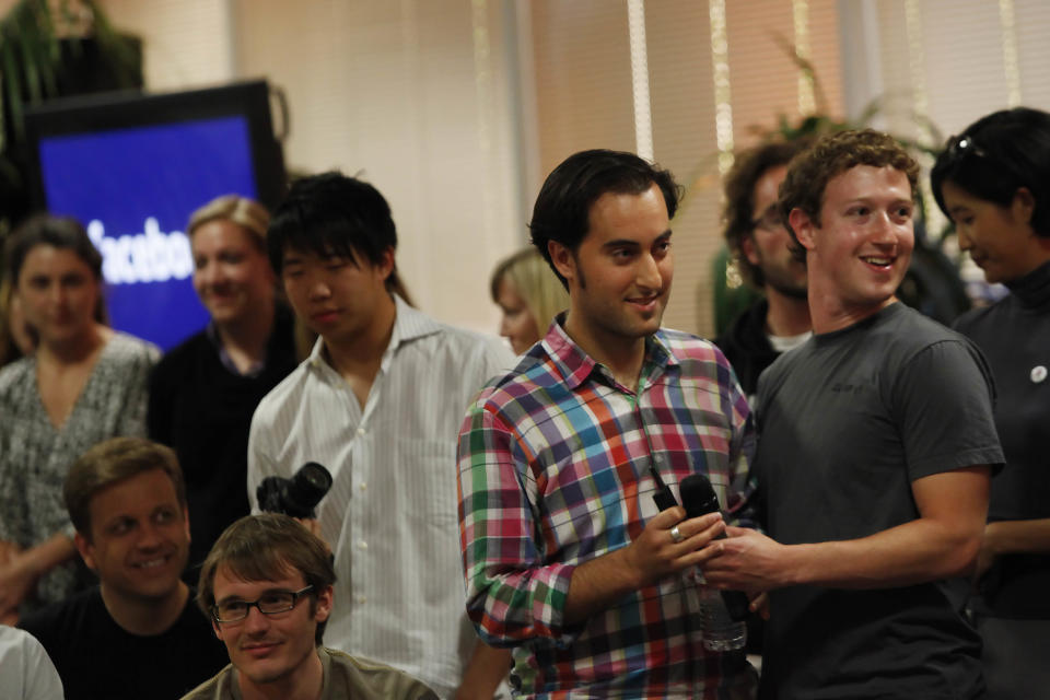 A group of people, including one in a plaid shirt and another in a plain t-shirt, smiling and interacting at an indoor event