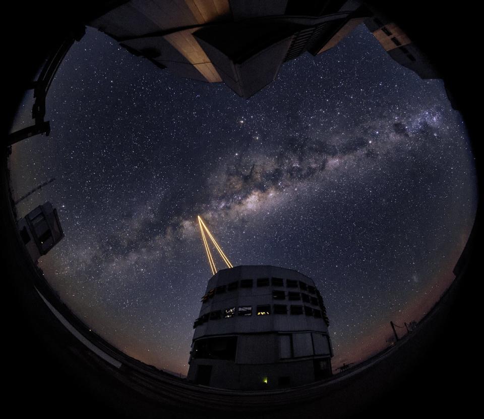 four yellow beams of light shoot up into a starry night sky from a cylindrical building