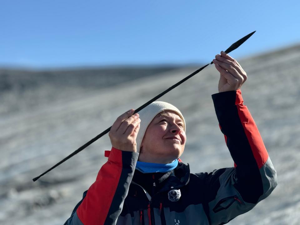 researcher in warm clothing holds up an ancient arrow and arrowhead on a rocky mountainside