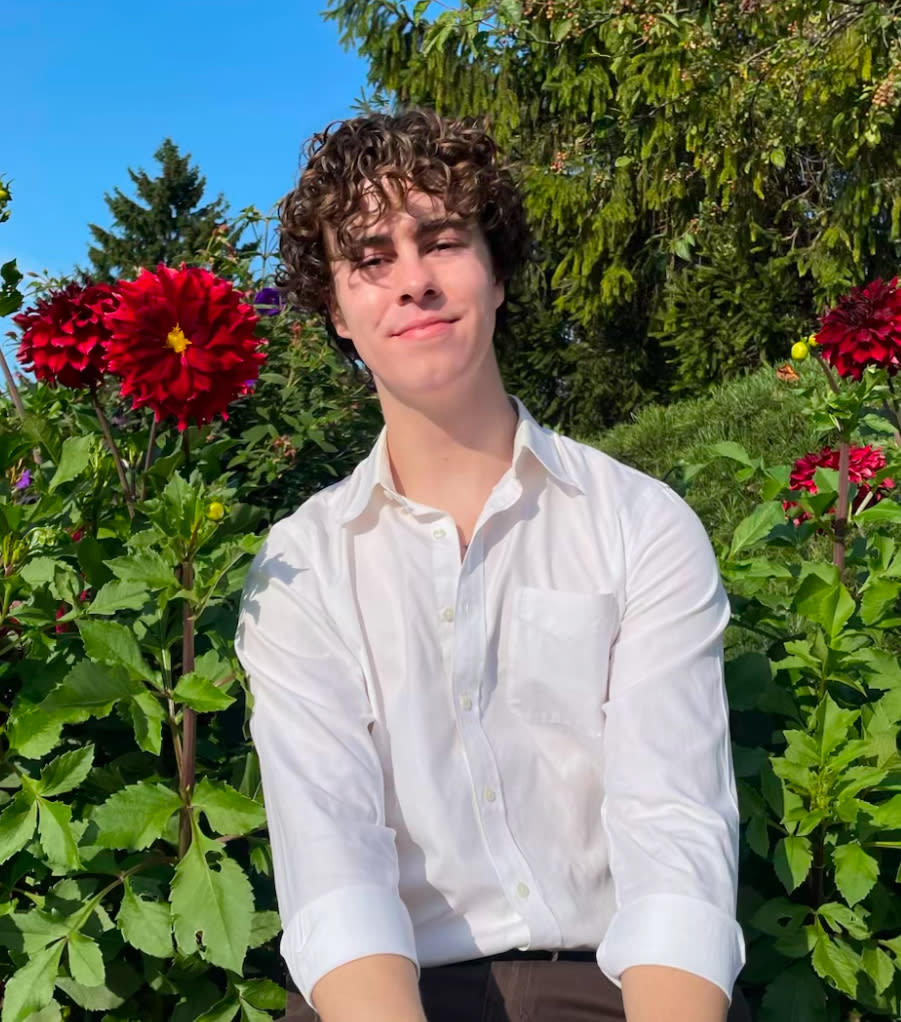 Person in a white shirt smiles while seated among large blooming flowers in a garden setting