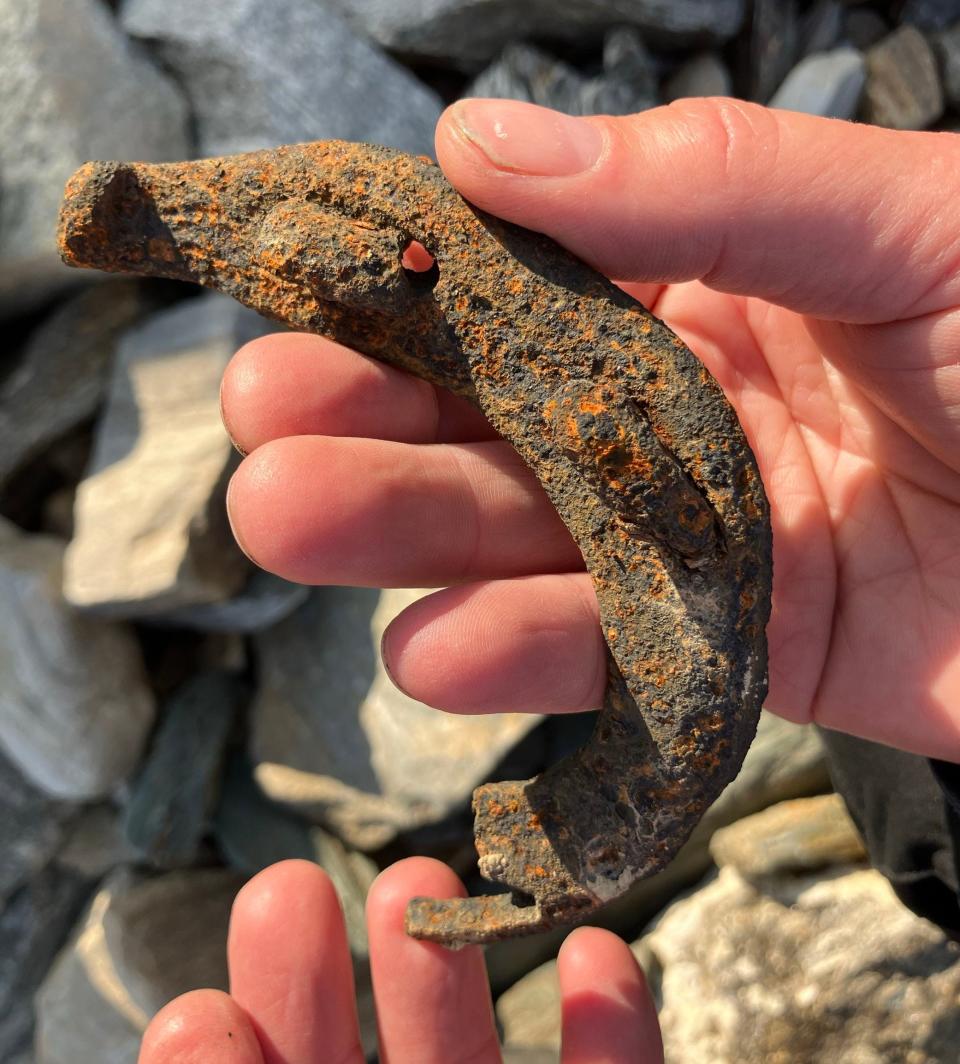 rusty orange-speckled rough horseshow fragment curved in a person's hands above a pile of rocks