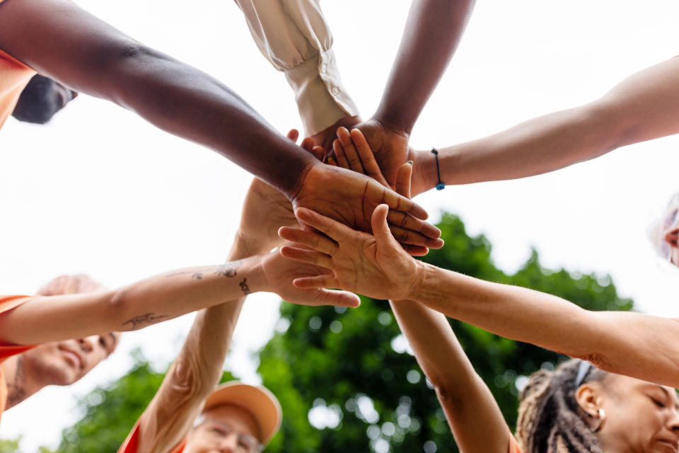 A diverse group of people forming a supportive circle with hands stacked together, showcasing teamwork and unity