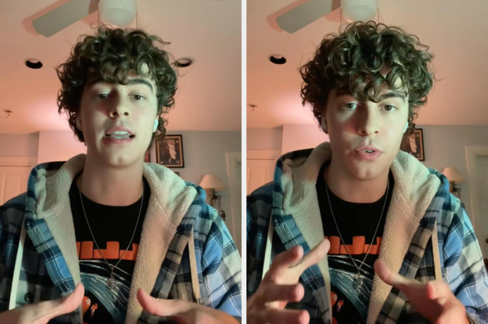 A person with curly hair wearing a plaid shirt over a graphic tee talks while gesturing with hands, indoors