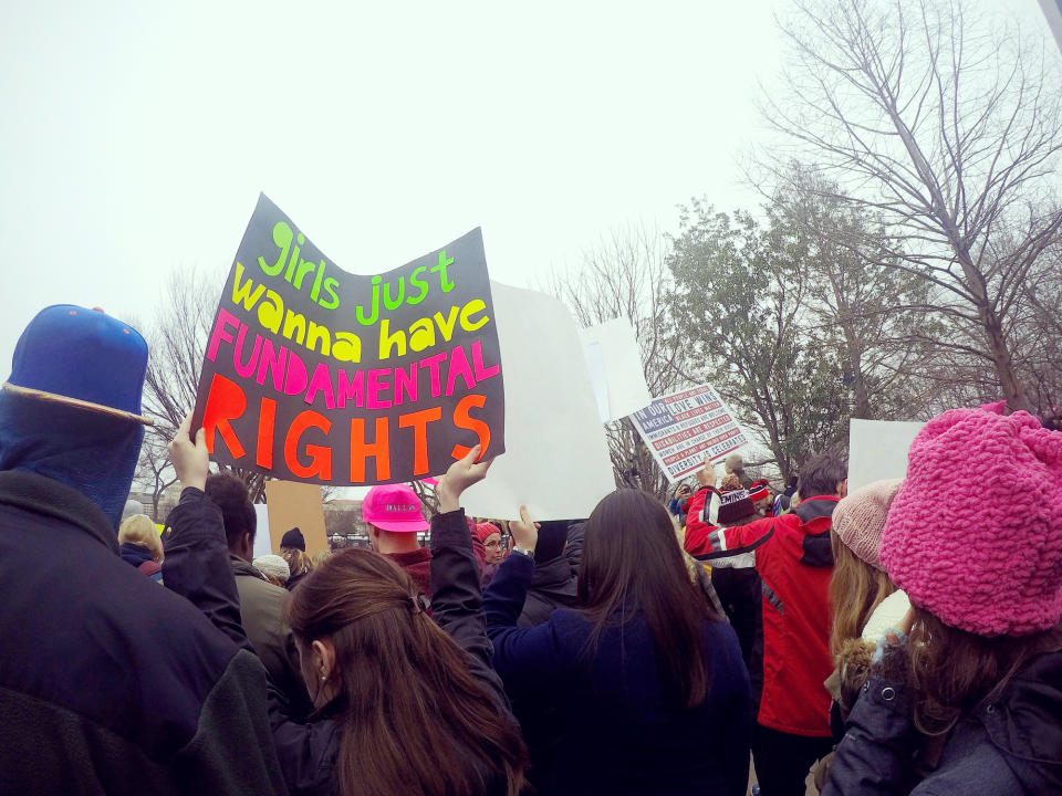 People at a rally holding signs, including one that reads, "Girls just wanna have fundamental rights." Crowd is diverse and bundled up for cold weather