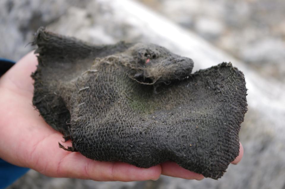 ancient muddy rough-fabric mitten held in the palm of someone's hand