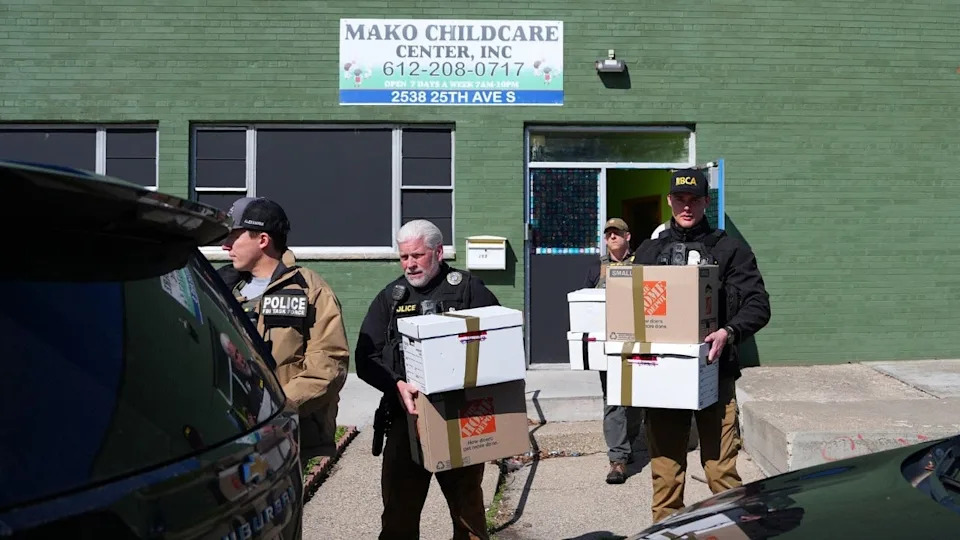 Federal agents carry boxes out of a green building